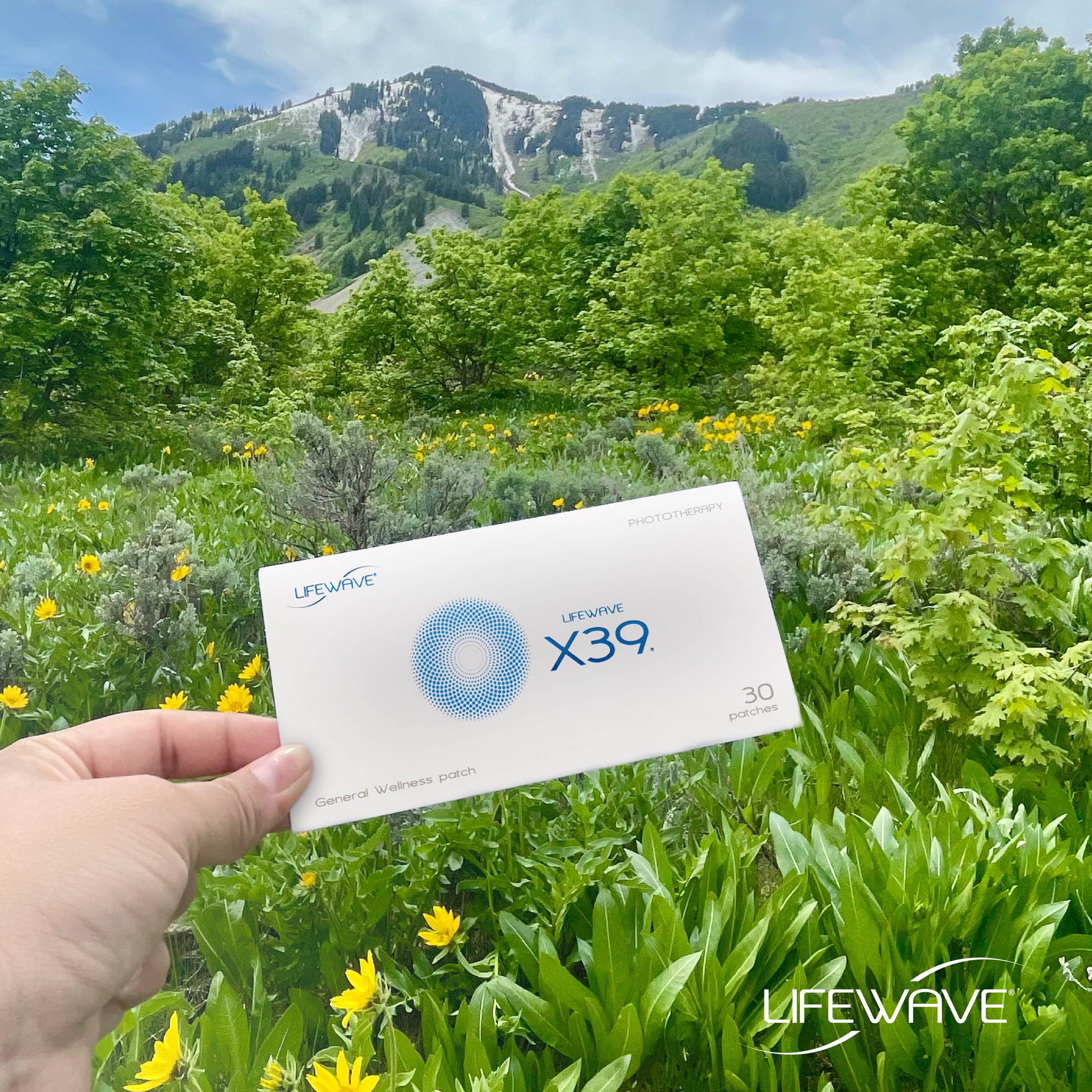 Hand holding Lifewave X39 patch in lush mountain setting