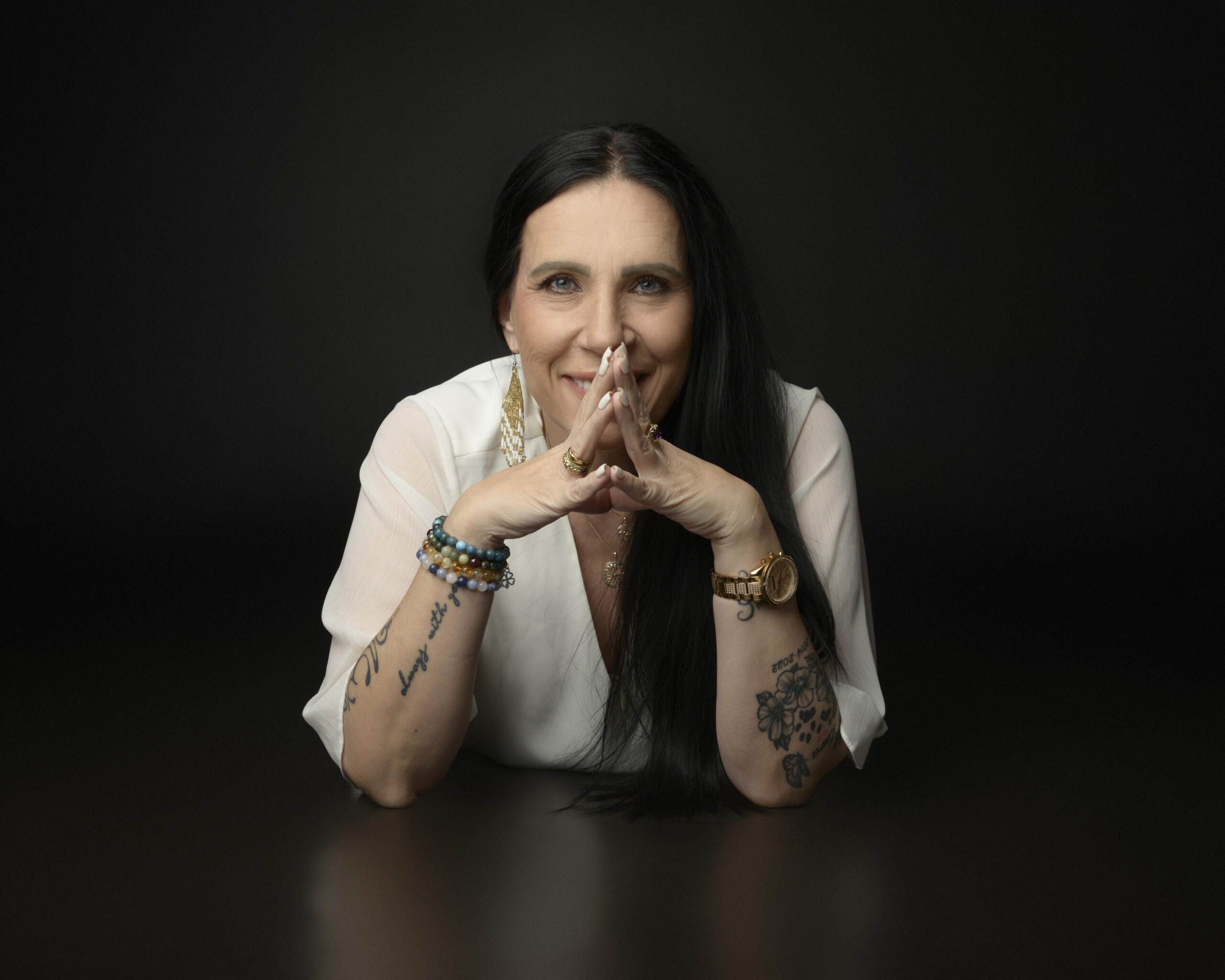 Smiling woman with tattoos posing on dark background.